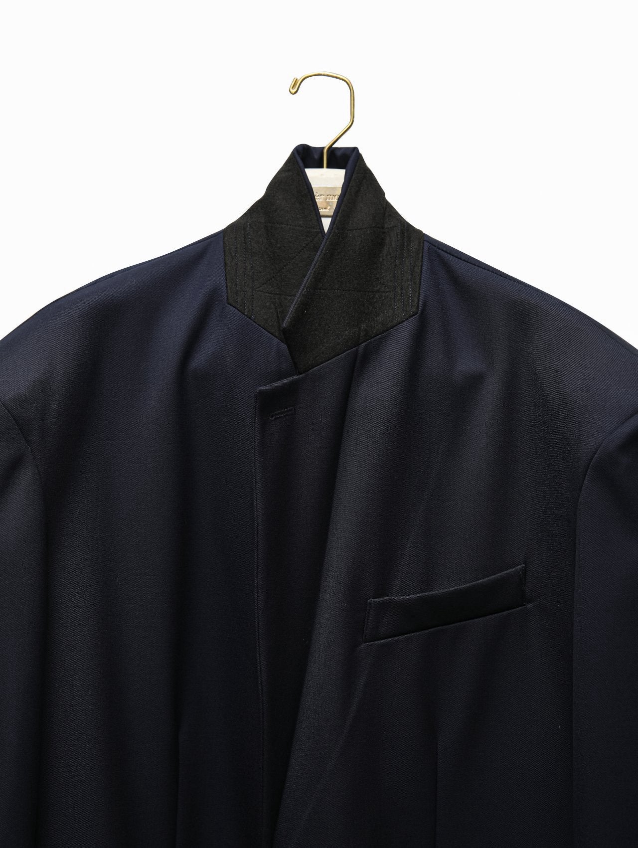 Close-up of navy blazer’s collar with contrasting black felt underside and subtle vertical weave texture.
