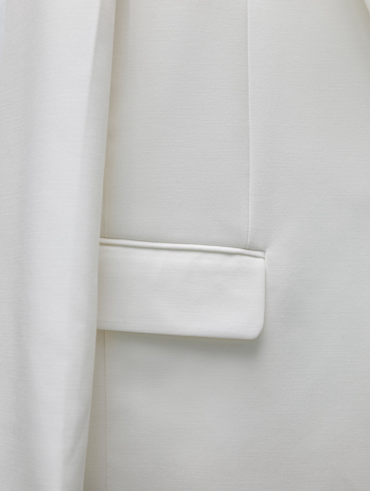 Detailed view of cream blazer’s flap pocket and textured fabric finish