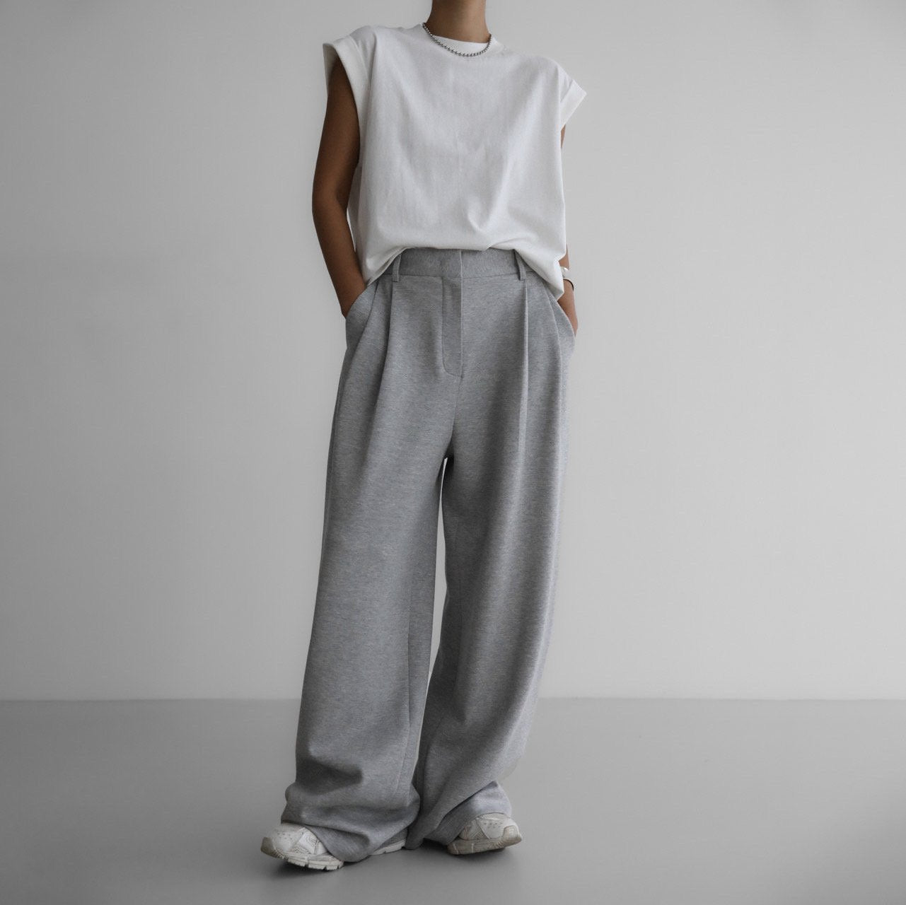 Front-facing full-body look featuring gray wide-leg pants and shoulder-padded white top for a modern, relaxed profile.