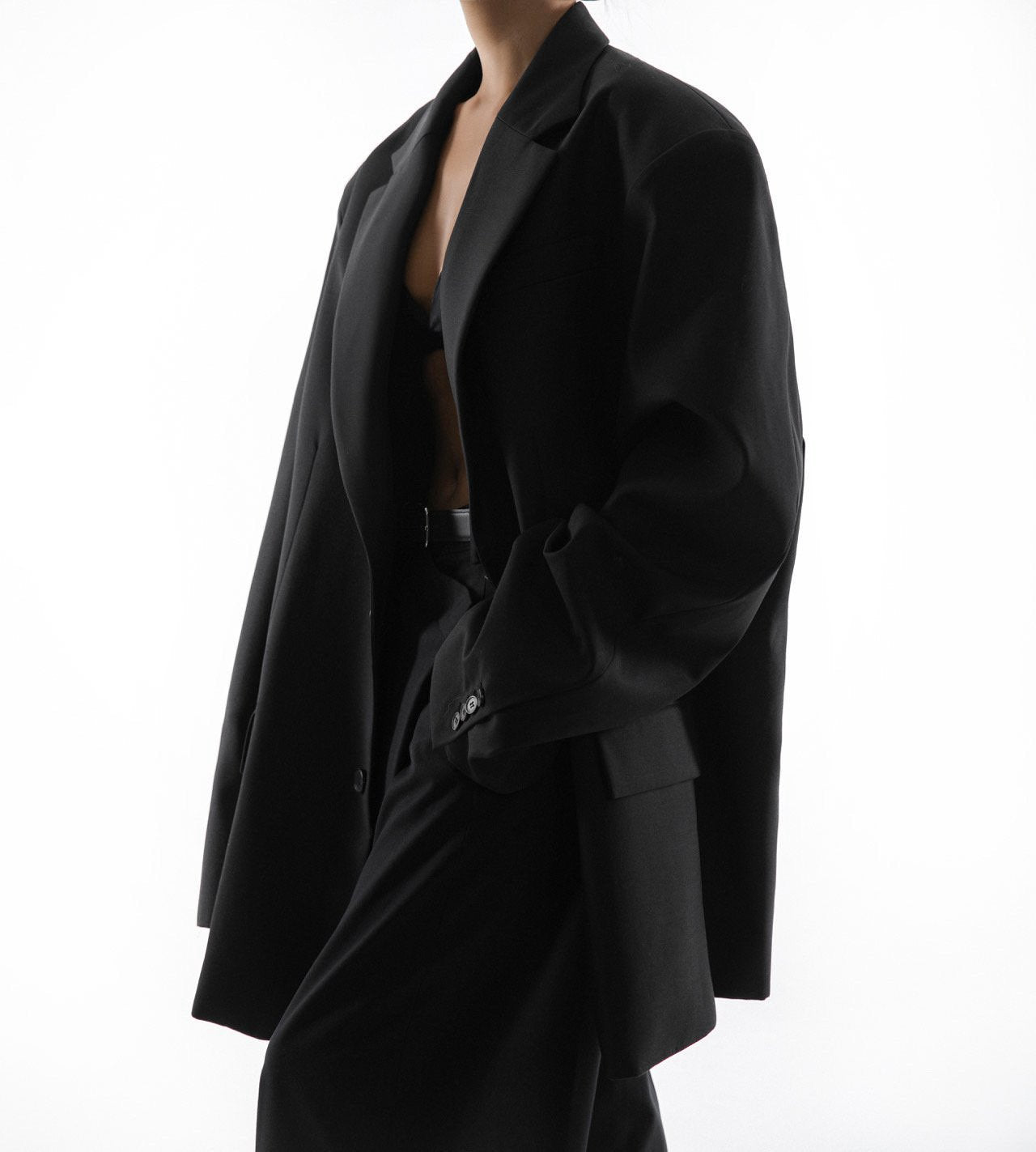 Model turned to side wearing oversized black blazer with structured shoulders and minimal layers