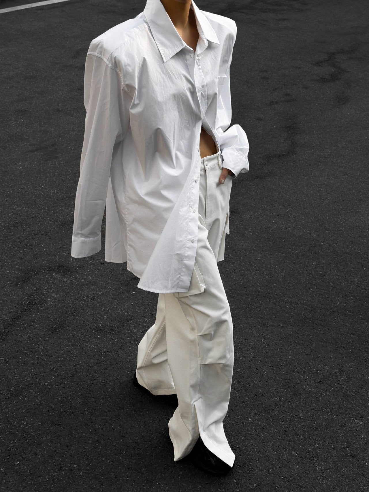 Model mid-walk wearing oversized white shirt with untucked hem and low-buttoned styling