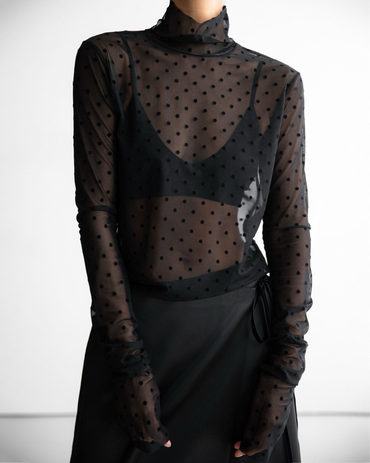 Model wearing a fitted black mesh turtleneck with polka dots over a bralette