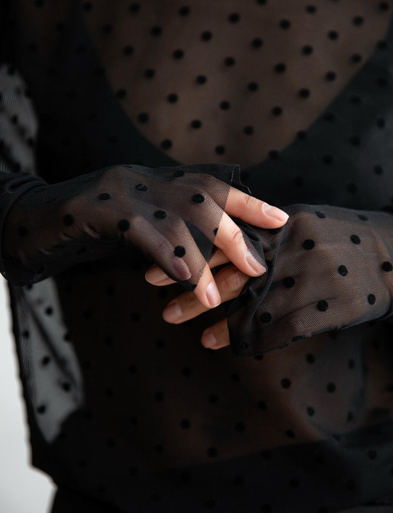Detailed view of hands through semi-sheer black mesh polka dot sleeves