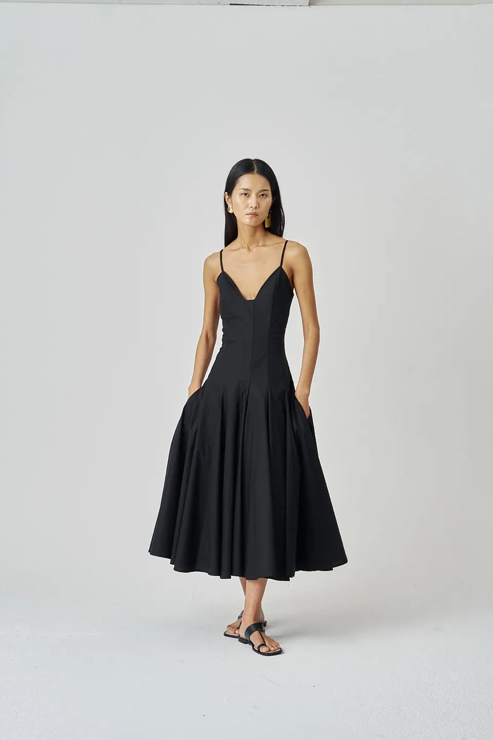 Studio shot of a black cotton midi dress styled with simple sandals and subtle gold accents.