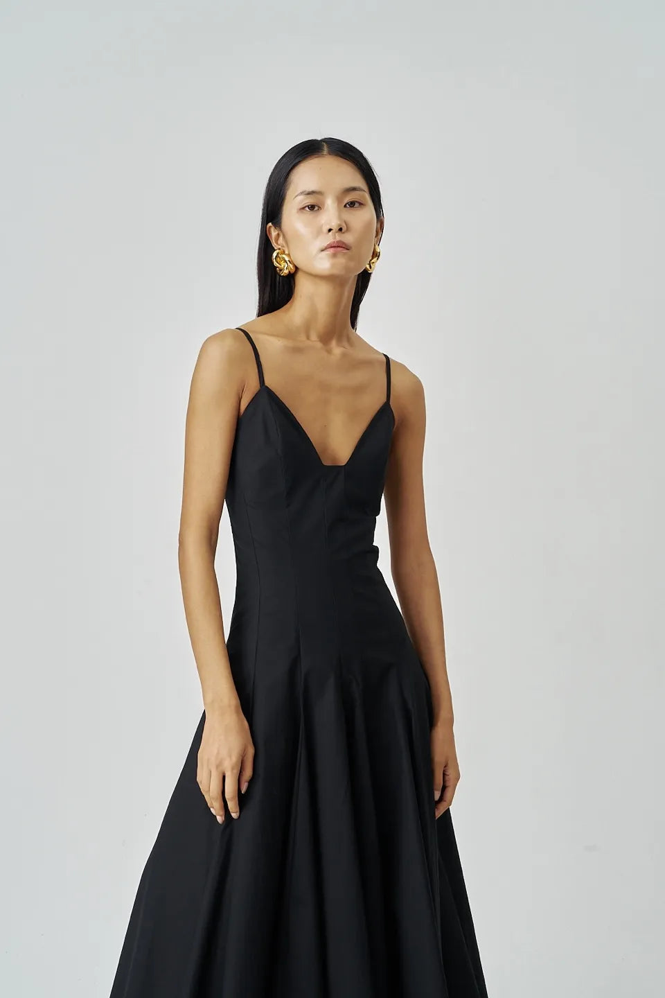 Cropped front portrait of black A-line midi dress featuring a deep neckline and tailored bodice.