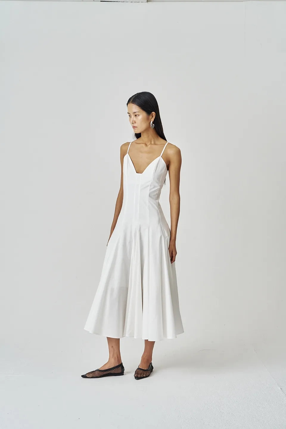 Model wearing an ivory A-line midi dress with slim straps and flared skirt.