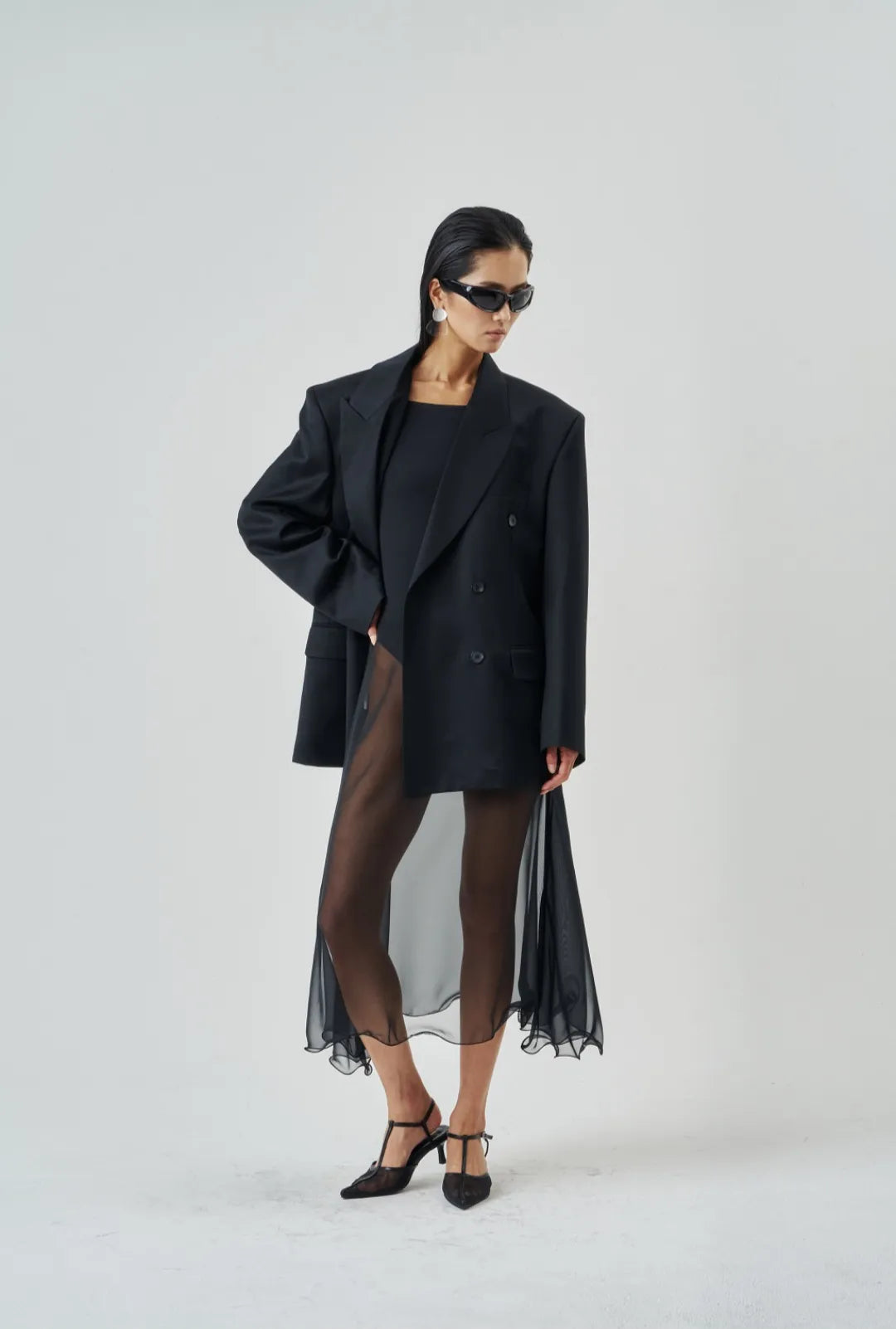 Model standing in profile wearing a flowy sheer midi skirt with wired hem and black pointed heels