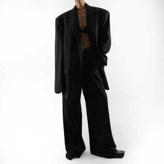 Relaxed pose in oversized black blazer and matching black trousers, styled with minimal underlayer