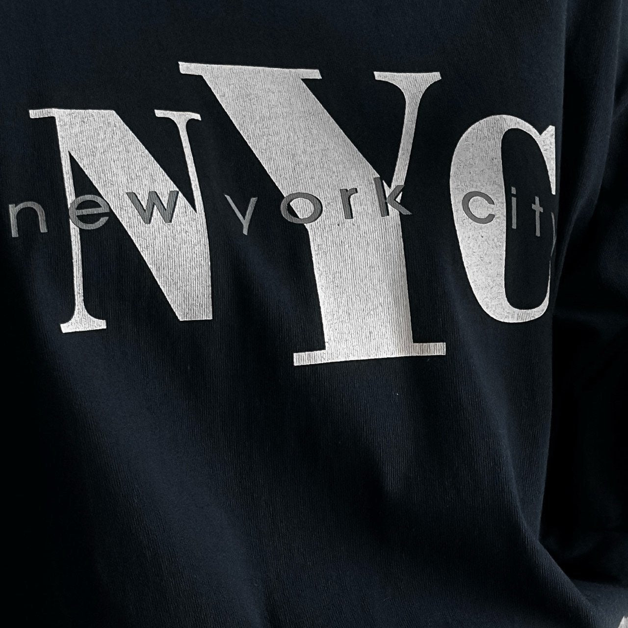 Close-up of bold NYC New York City white typographic print on navy oversized t-shirt.