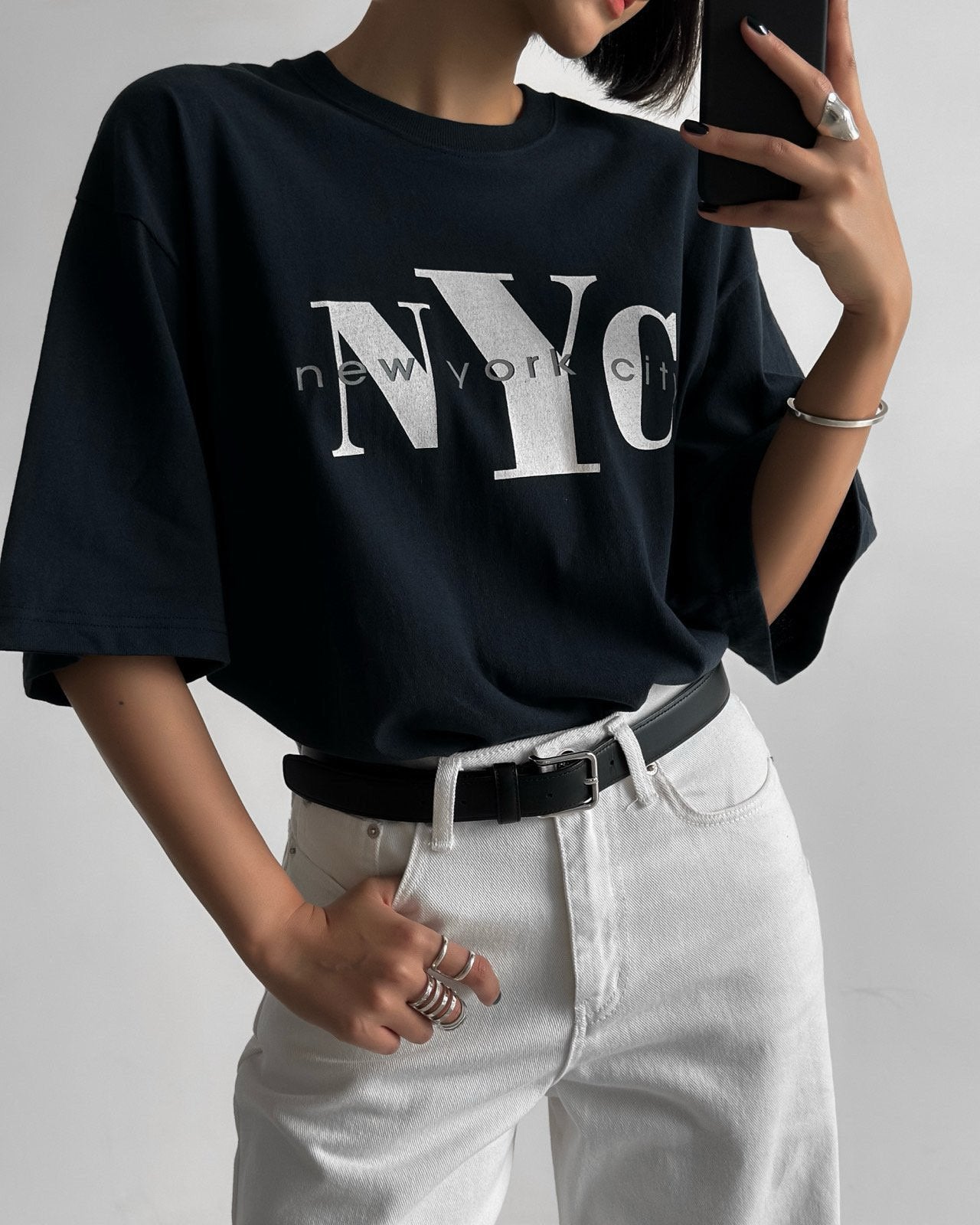 Oversized navy NYC graphic t-shirt styled with white pants and black belt, shot from waist up