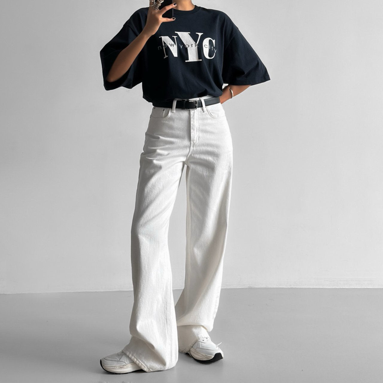 Model wearing oversized navy NYC print t-shirt with white wide-leg pants — minimalist streetwear style.