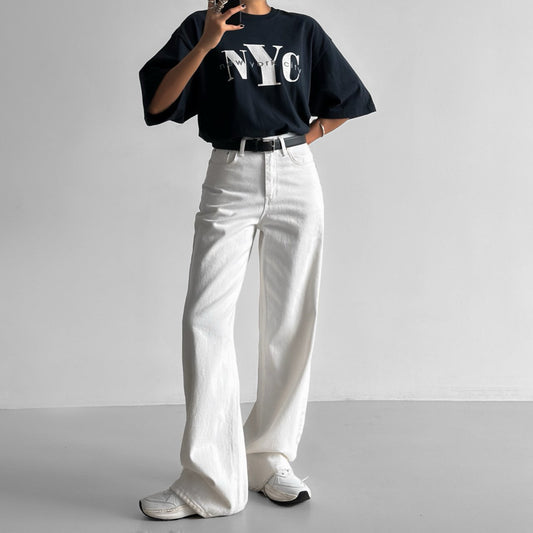 Model wearing oversized navy NYC print t-shirt with white wide-leg pants — minimalist streetwear style.