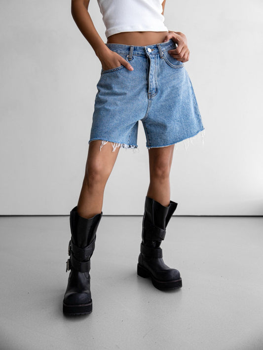 Model wearing high-rise frayed denim shorts with black moto boots