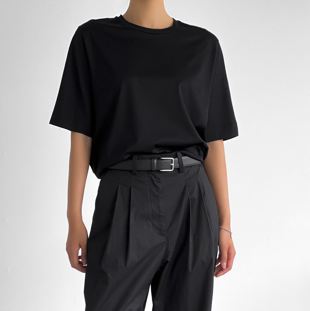Full front view of model in black oversized t-shirt styled with high-waisted pleated trousers