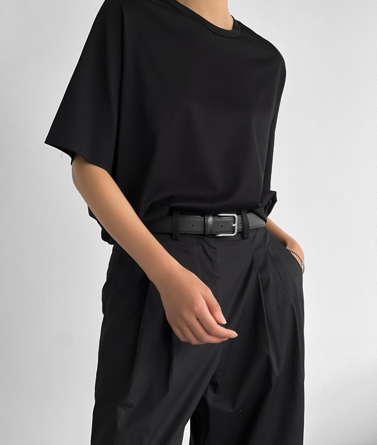 Close-up of model wearing a black oversized t-shirt tucked into pleated black trousers with a belt