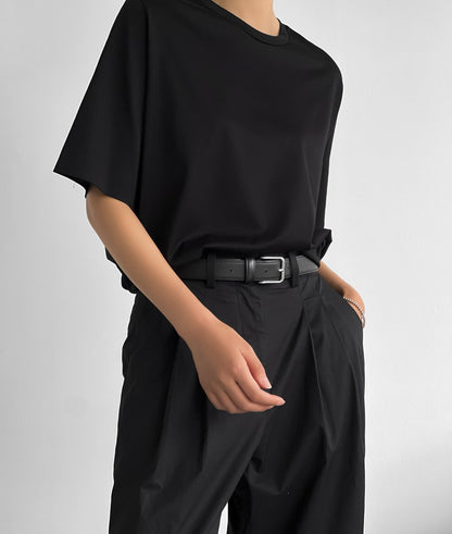 Close-up of model wearing a black oversized t-shirt tucked into pleated black trousers with a belt