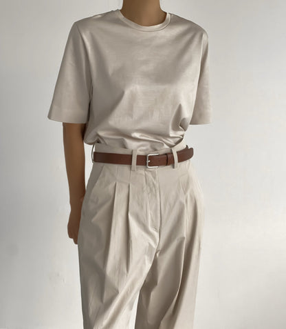 Front view of a sleek, oversized light beige t-shirt tucked into tailored pleated pants, styled with a chocolate brown belt.