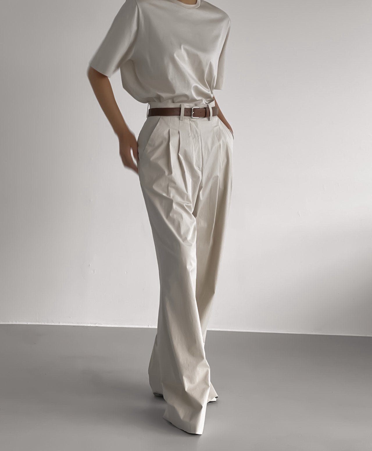 Full-body image showcasing flowy light beige trousers paired with a tonal tee and structured belt in a refined monochrome palette.