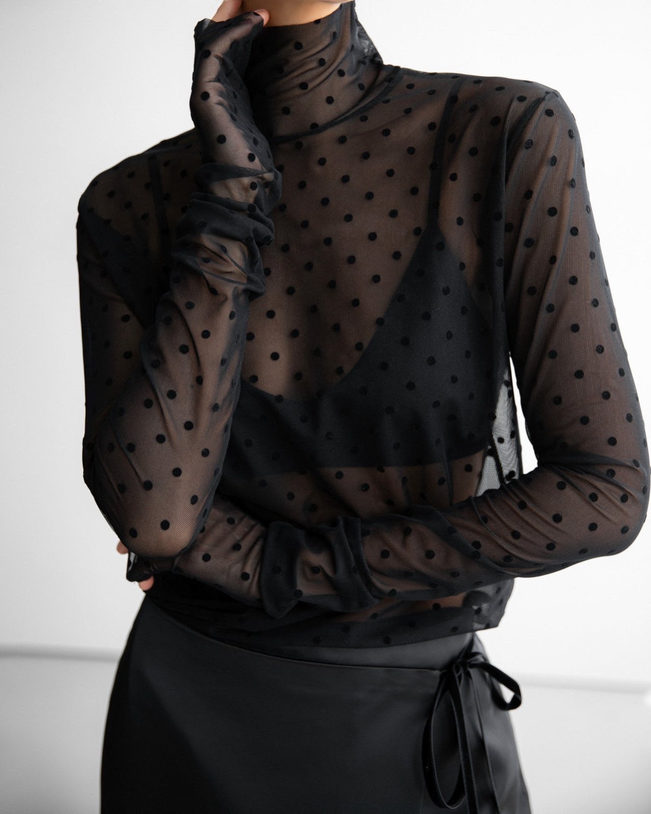 Close-up of a black sheer polka dot mesh turtleneck top with ruched sleeves
