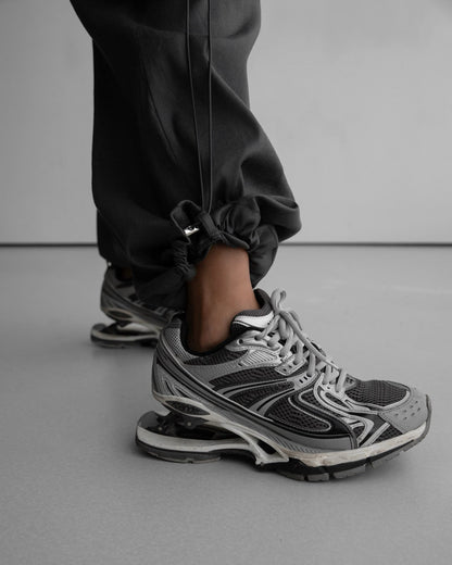 Detail shot of elastic drawstring hem and hardware toggle on the pants, worn with sculptural grey athletic sneakers.