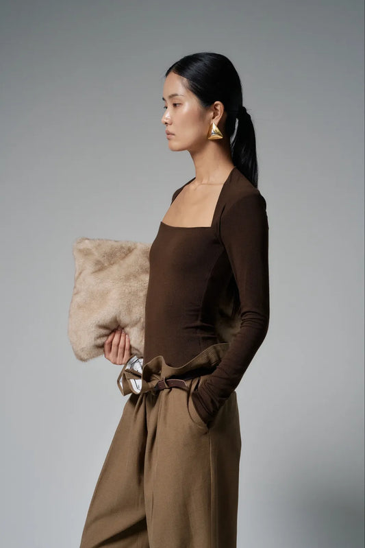 Side profile of model Model wearing the top in chocolate brown, paired with wide tailored trousers.
