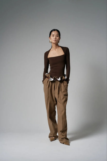 Model wearing the top in chocolate brown, paired with wide tailored trousers, front view.