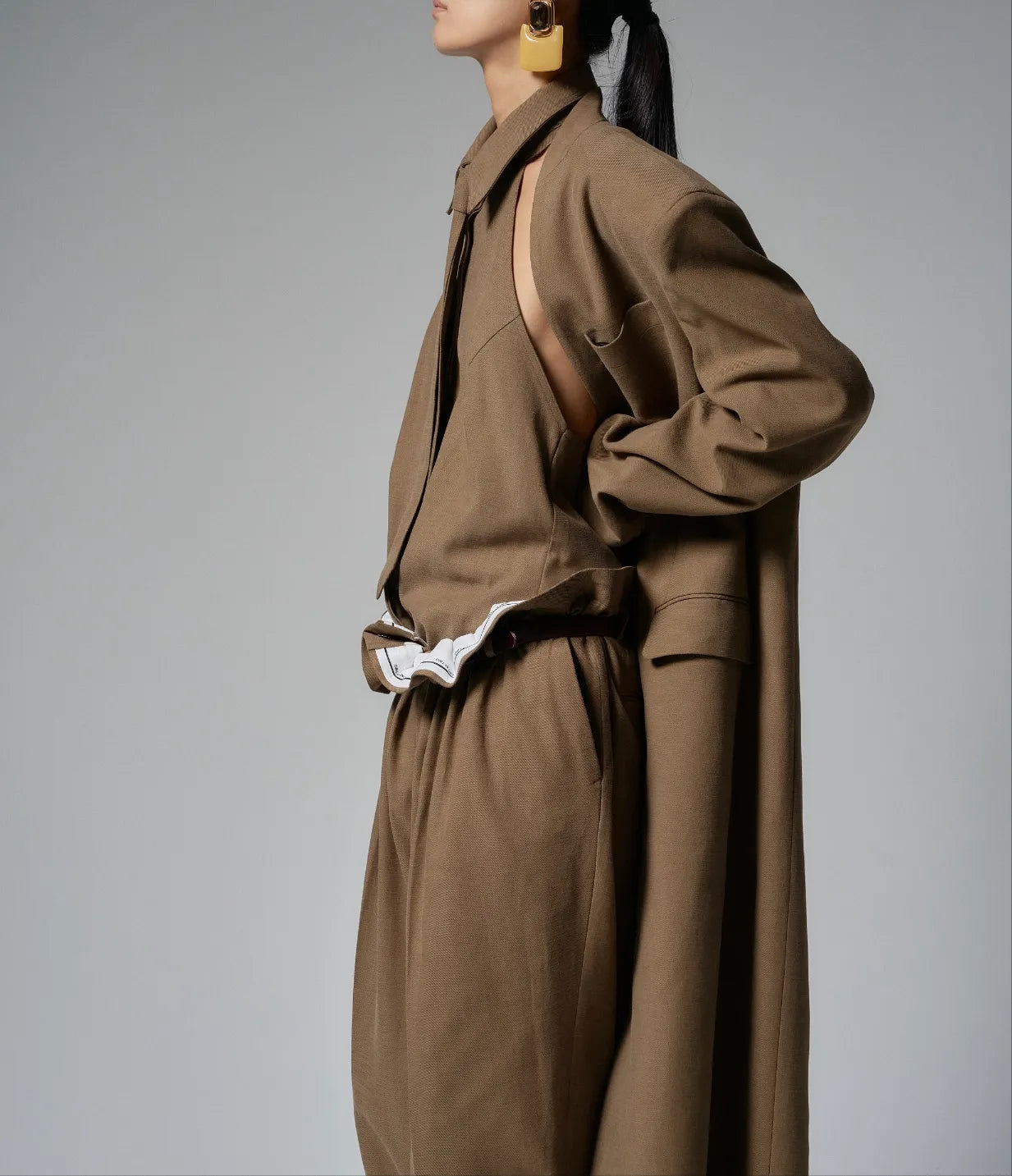 Beige tie-front halter shirt layered under an oversized coat, highlighting its minimalist draped design.