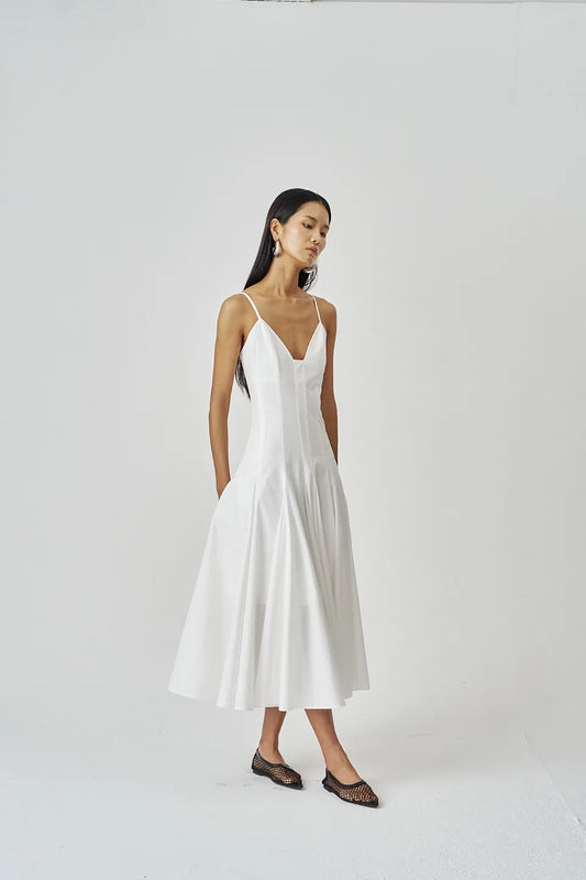 Model wearing an ivory structured midi dress with a flared hem and slim straps, styled with mesh flats in a minimalist studio setting.