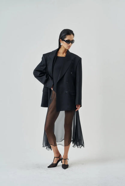 Model standing in profile wearing a flowy sheer midi skirt with wired hem and black pointed heels