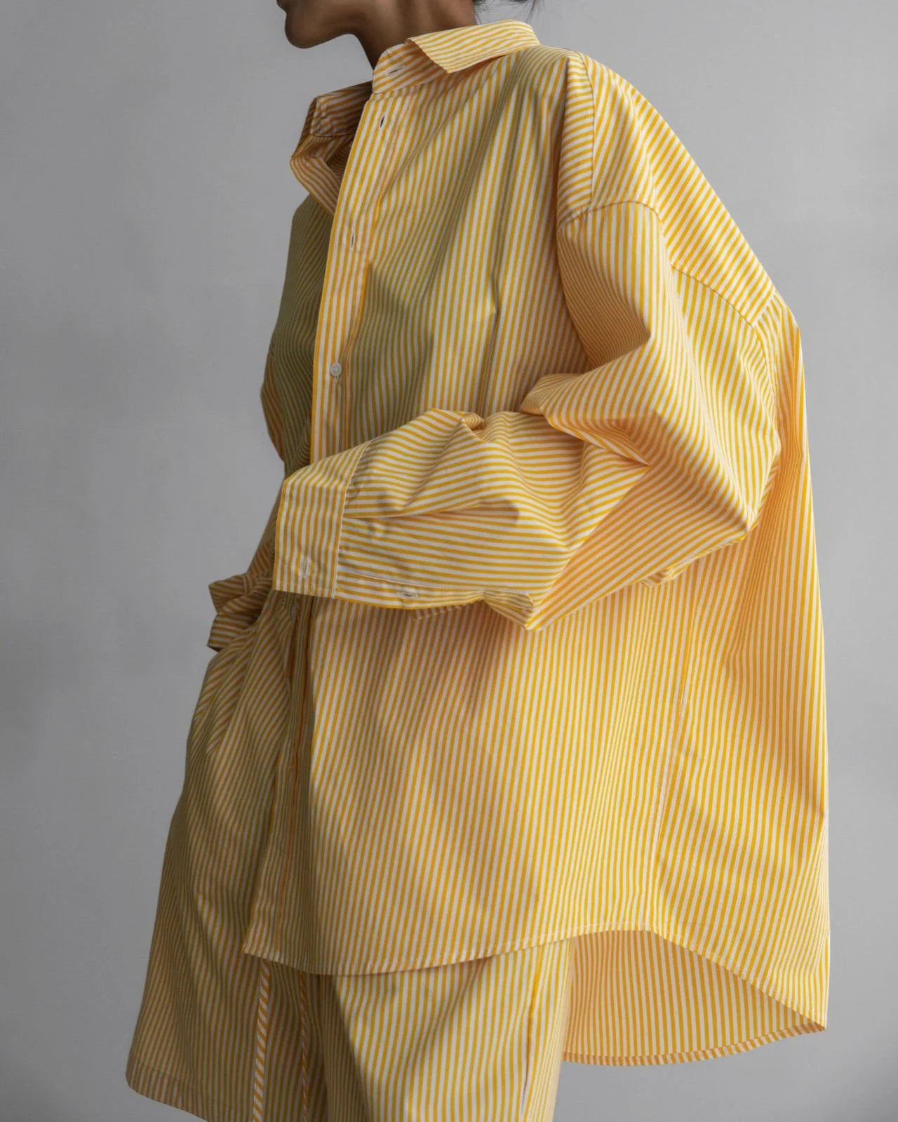 Side profile showcasing the relaxed silhouette and drop shoulder design of the yellow striped shirt.
