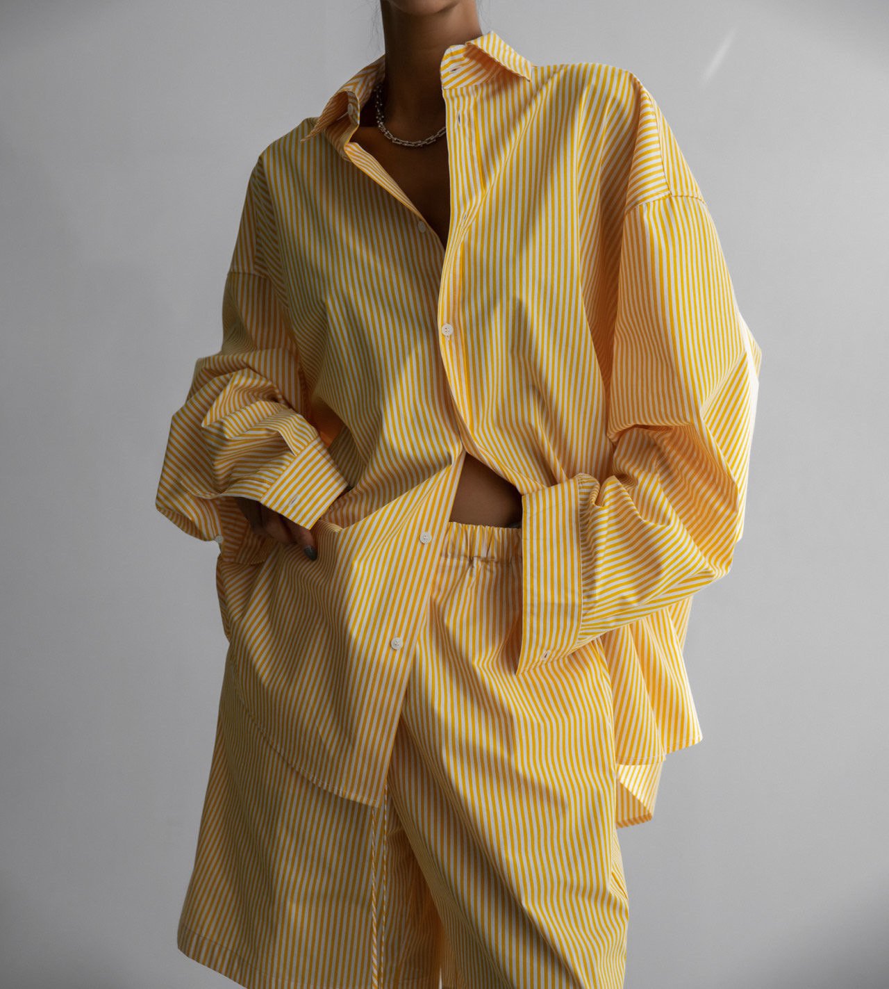 Model styling the oversized yellow striped set with unbuttoned shirt to reveal high-waisted matching shorts.

