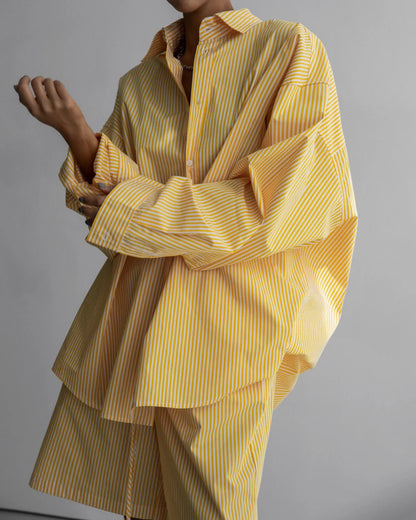 Close-up of a model wearing an oversized yellow and white striped button-down shirt with exaggerated cuffs.