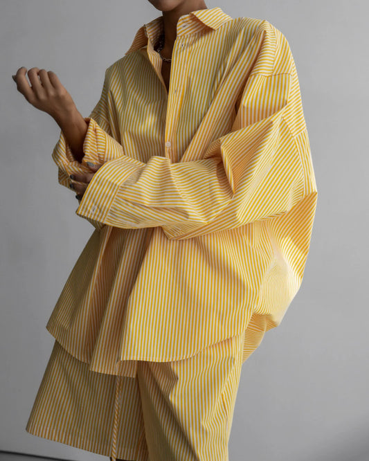 Close-up of a model wearing an oversized yellow and white striped button-down shirt with exaggerated cuffs.
