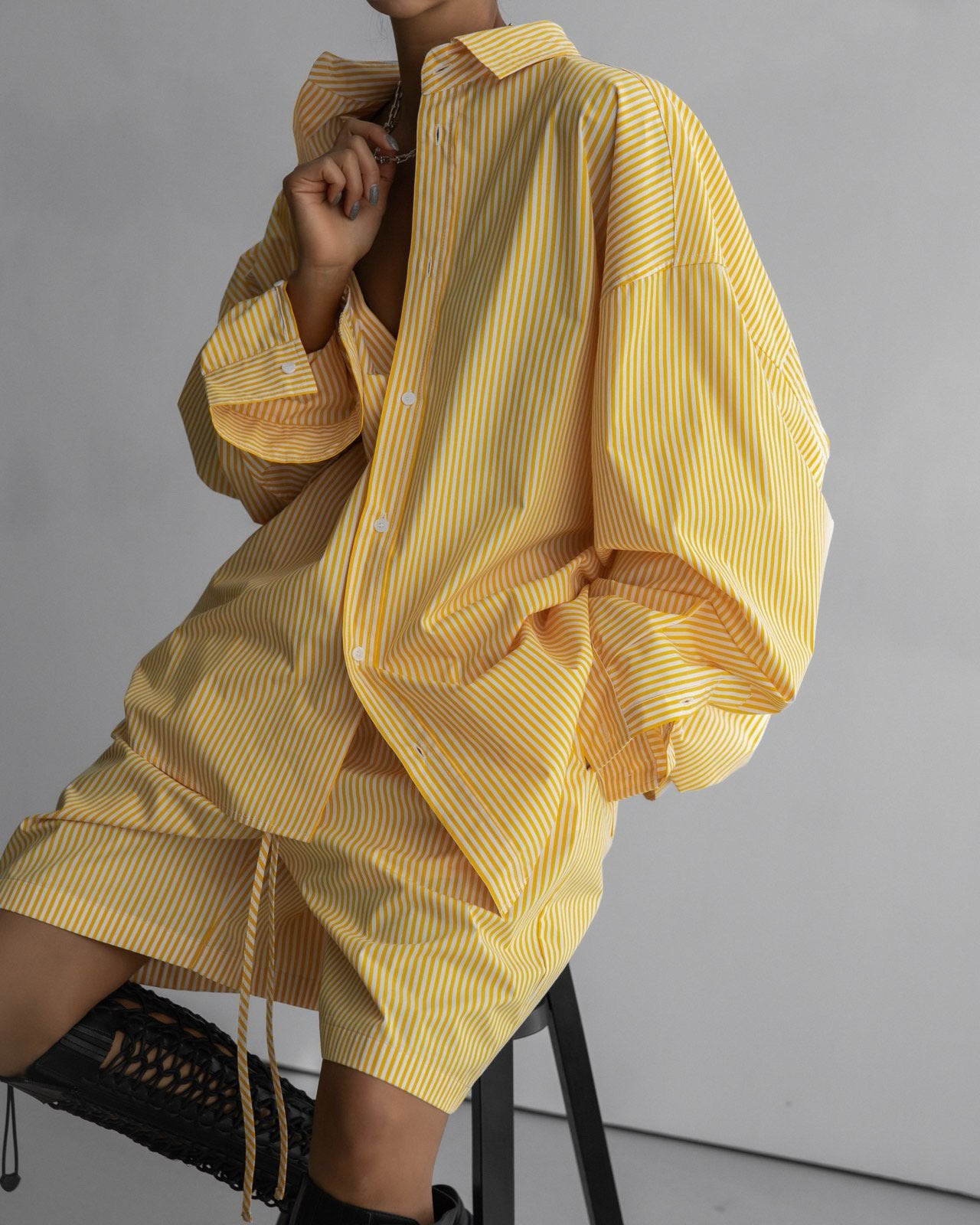 Seated model in a yellow striped co-ord set styled with statement black boots, highlighting the bold yet breezy look.