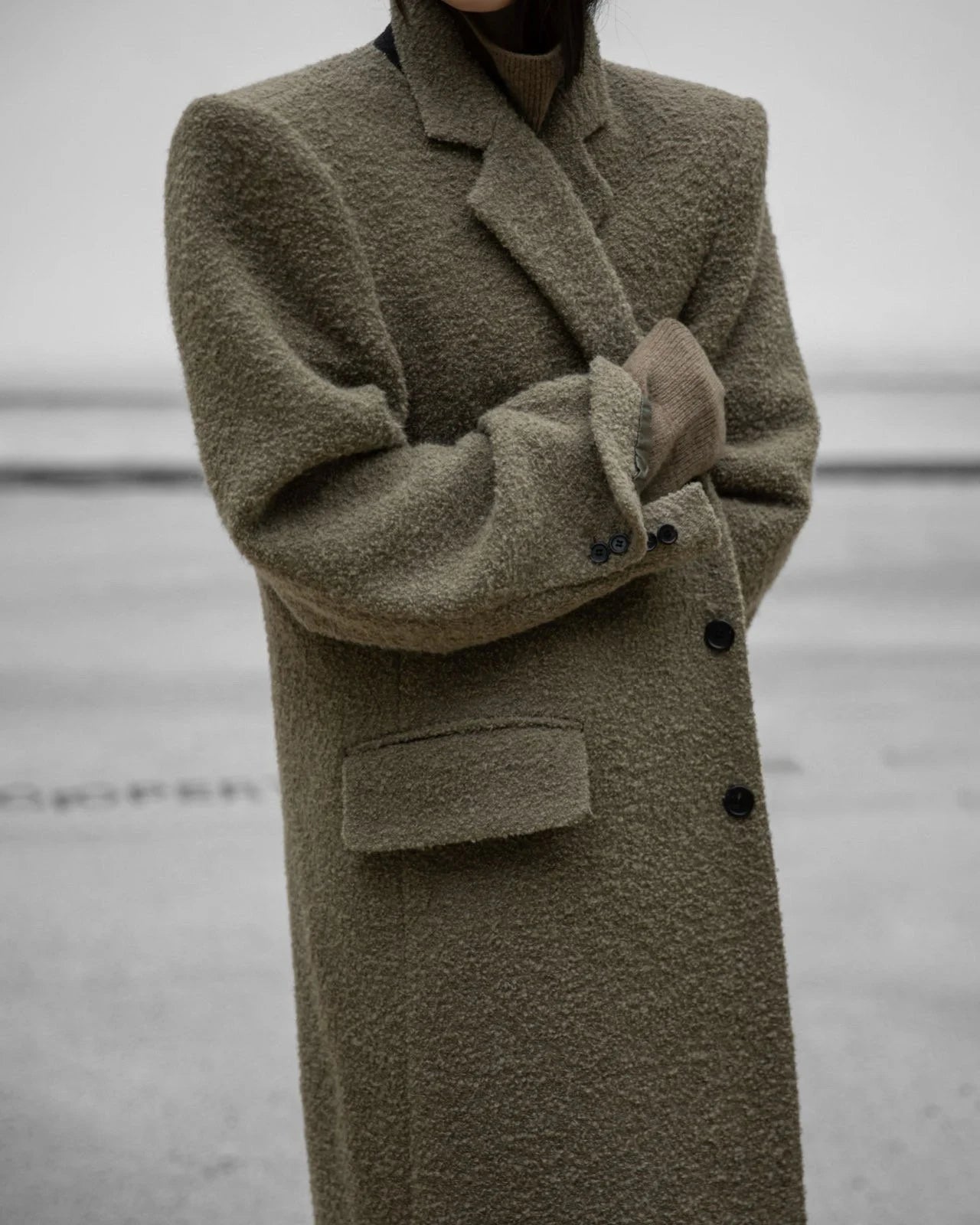 Side view of khaki beige bouclé oversized wool coat with structured shoulders.