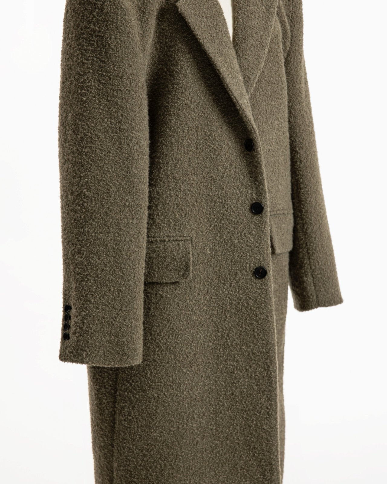 Close-up of khaki beige bouclé alpaca wool coat highlighting textured fabric, welt pockets, and black three-button front.
