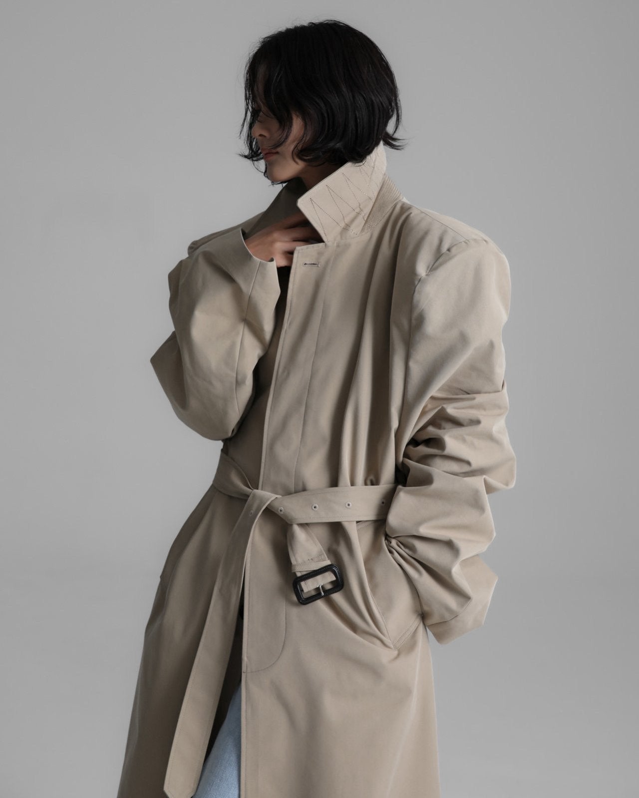 Side profile of the trench coat cinched at the waist with matching fabric belt and matte buckle.