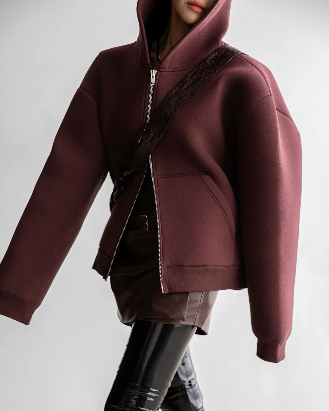 Model wearing structured oversized burgundy neoprene hoodie with zip closure and sculptural hood