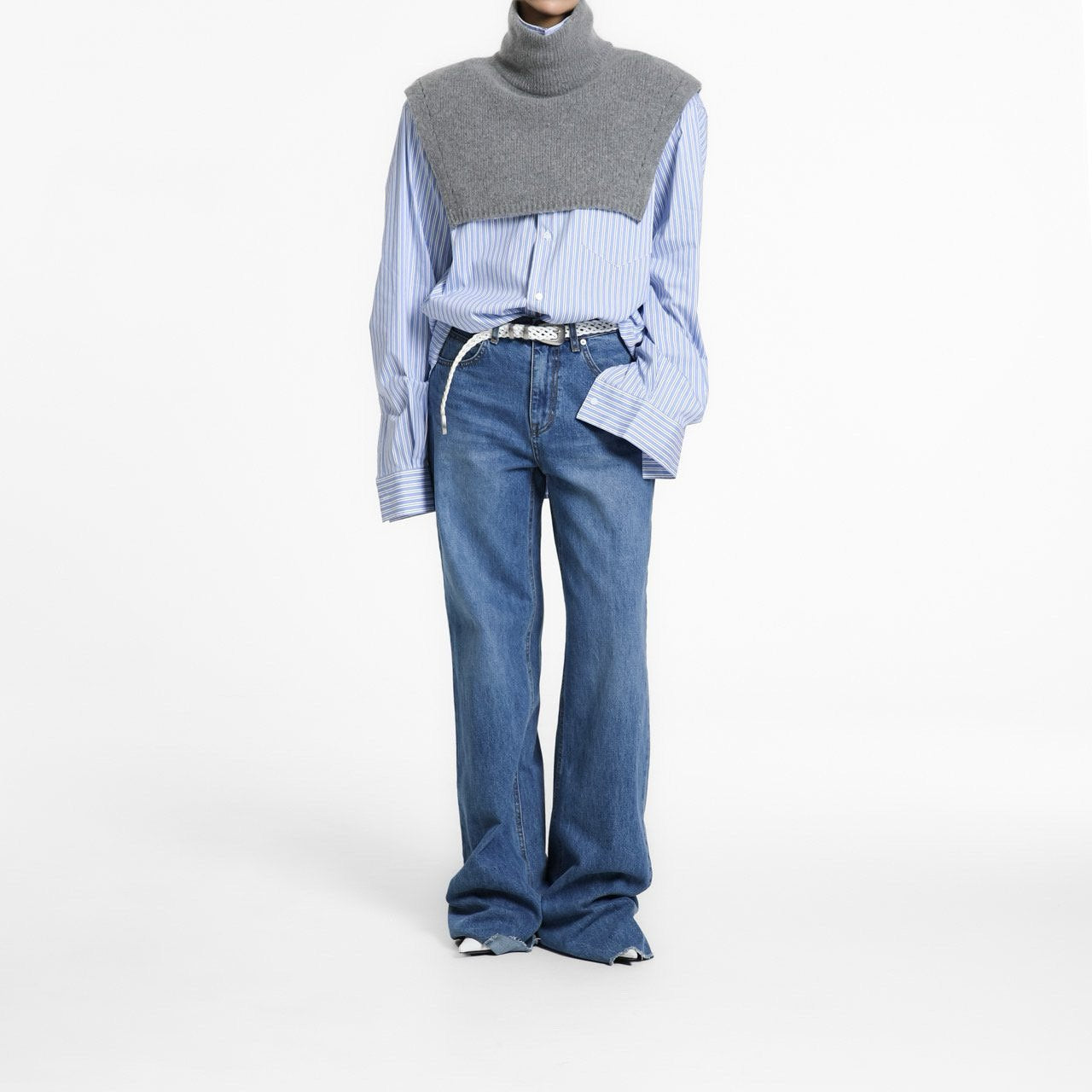 Model wearing the Turtleneck Wool Cape Knit layered over a blue striped shirt and denim, showcasing its sculptural cropped silhouette.