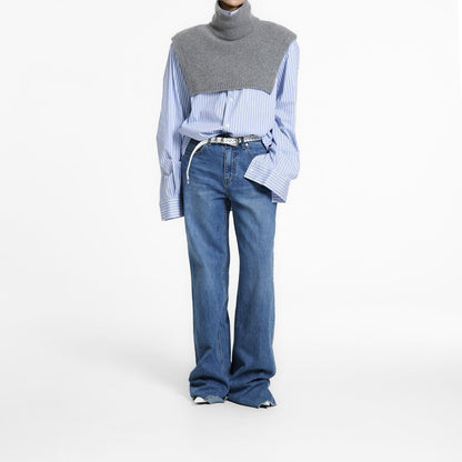 Model wearing the Turtleneck Wool Cape Knit layered over a blue striped shirt and denim, showcasing its sculptural cropped silhouette.