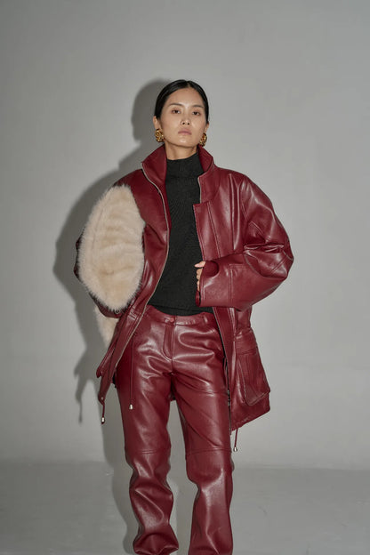 Model wearing oversized wine leather jacket with matching pants and black turtleneck in studio light.