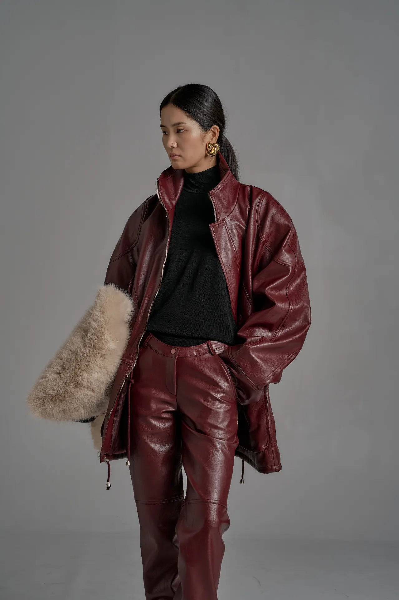 Side angle of burgundy leather jacket highlighting sculptural sleeves and relaxed fit.