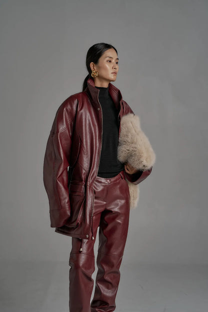 Three-quarter view of wine leather jacket with high collar and architectural seam detailing.