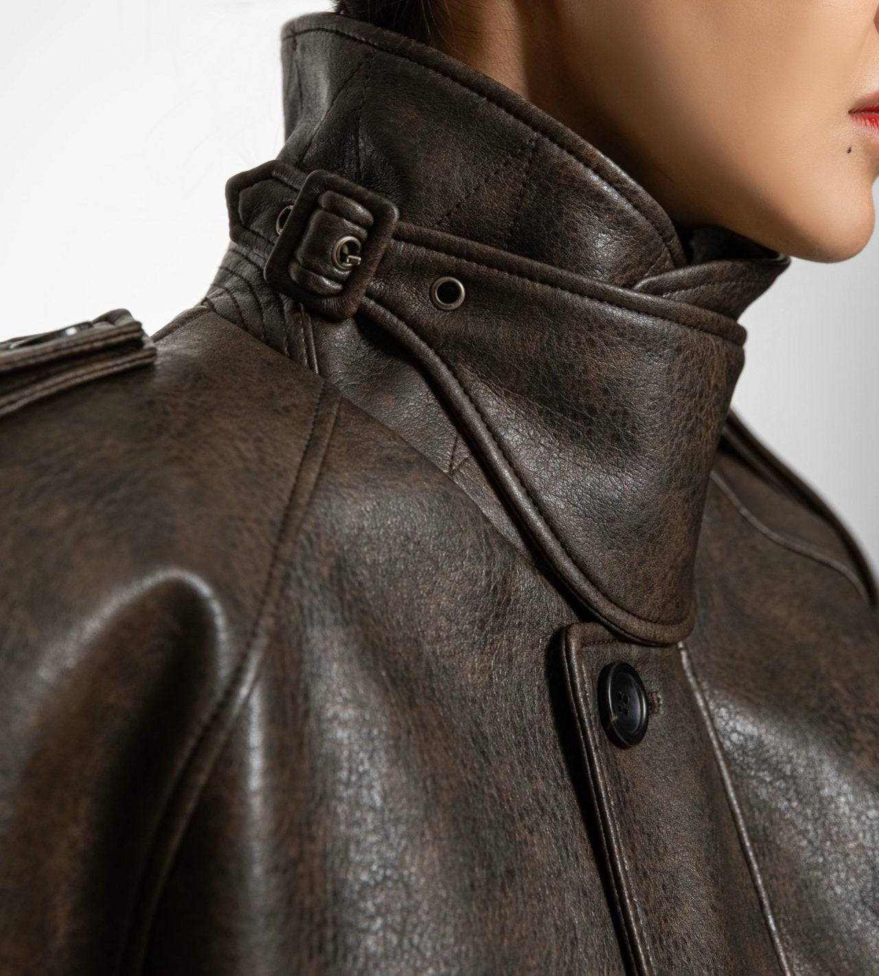 Close-up of sculpted high collar and matte button detailing on oversized vegan leather jacket