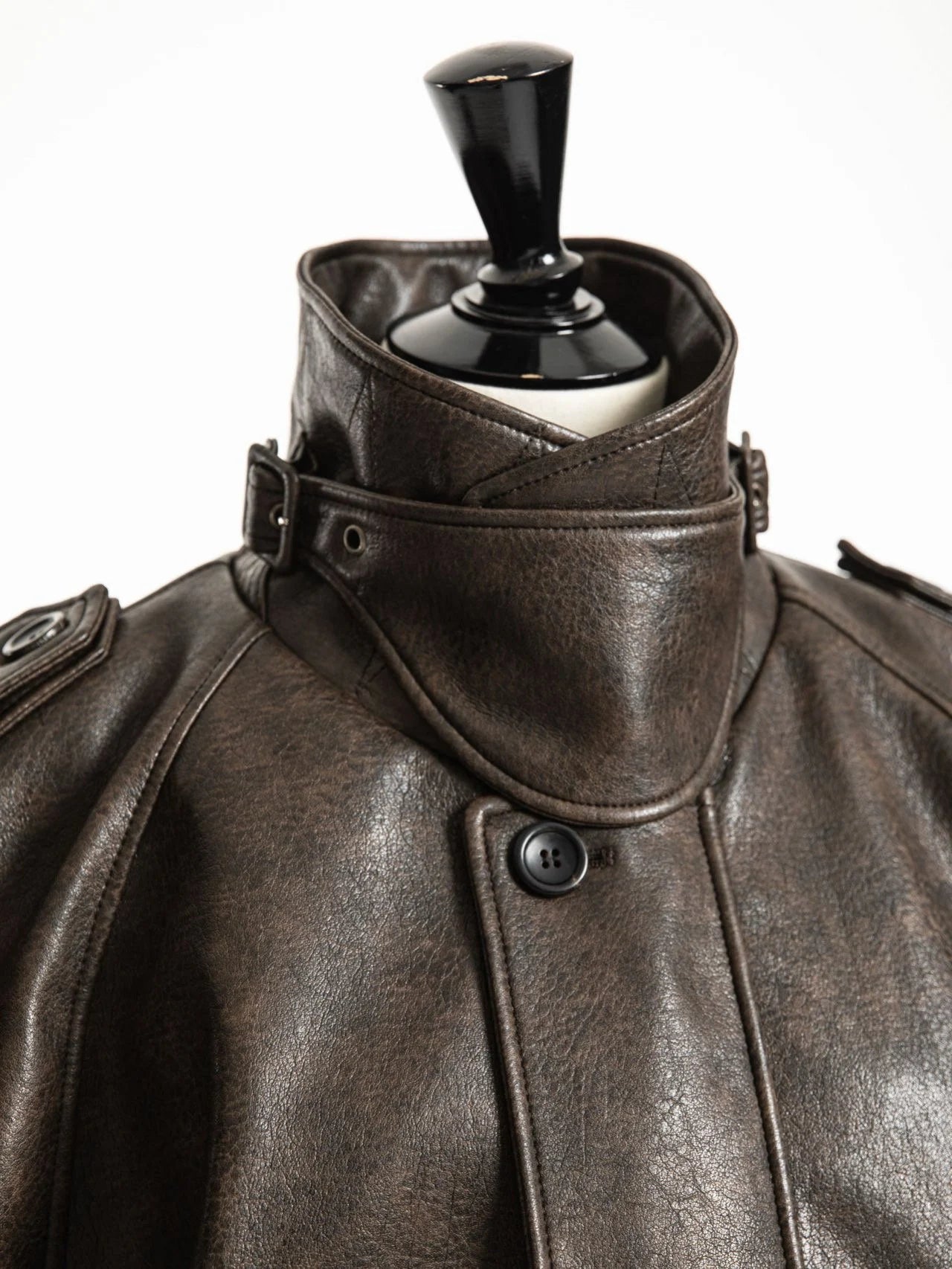 Close-up of sculpted high collar and matte button detailing on oversized vegan leather jacket