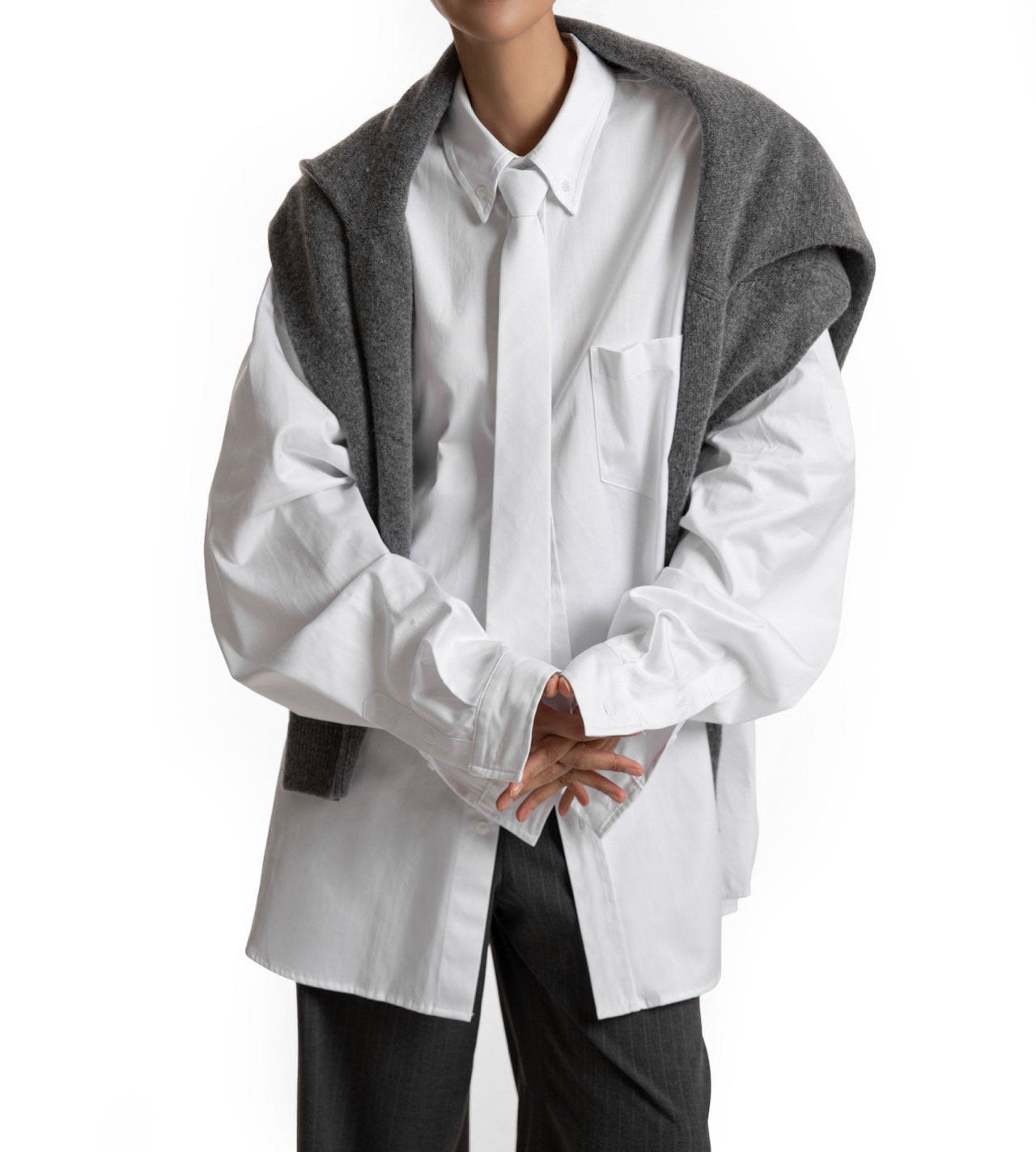 Oversized white shirt styled with gray knit over shoulders — relaxed modern silhouette.